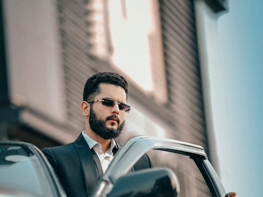A man in a dark suit and sunglasses stepping out of his car.